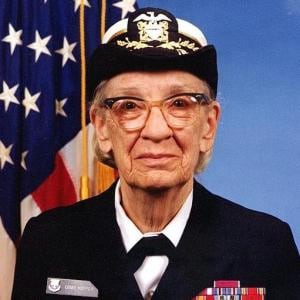 Grace Hopper profile picture. Grace wears her Navy uniform and stands in front of a US Flag