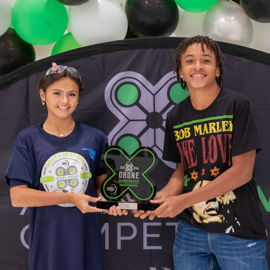 Two members of an Aerial Drone Competition team hold a trophy at an event.